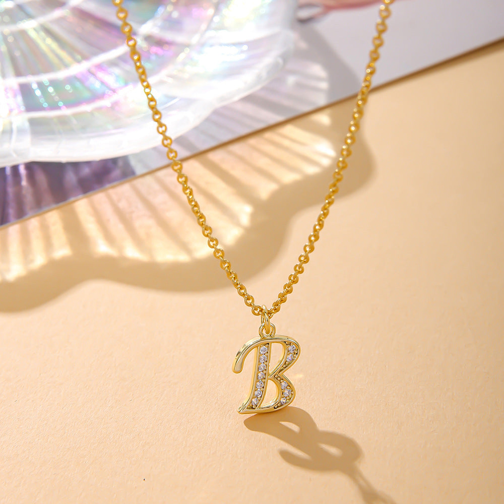 A K.Bola Fashion English necklace showcasing a B pendant with zircon inlay, hanging from an O-shaped alloy chain, graces a beige surface, framed by an iridescent shell.