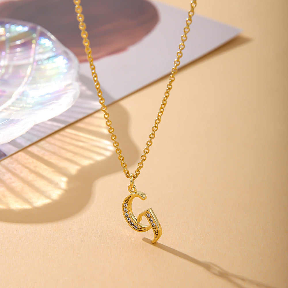 The K.Bola Fashion English 26 Letters Inlaid Zircon Copper Necklace for women features an O-shaped chain and a G pendant adorned with zircons. It rests on a neutral background under soft lighting with an iridescent shell shimmering behind.